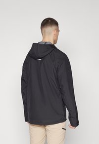 Veste noire imperméable avec capuche ajustée, manches longues et texture mate. Présente un logo sur le haut du dos et une coupe décontractée.