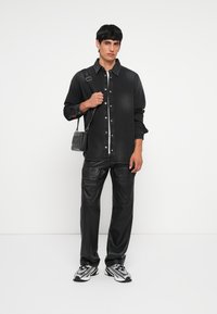 Chemise en denim noir avec fermeture à boutons, associée à un pantalon en simili cuir noir. Les accessoires incluent un sac à bandoulière texturé noir et des baskets argentées.