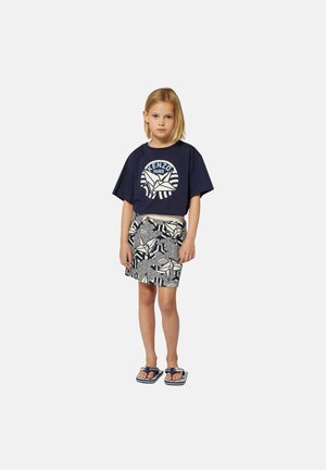 T-shirt bleu marine avec logo blanc, jupe à motifs bleu marine et crème, et tongs bleues. Tenue simple et décontractée adaptée aux températures chaudes.