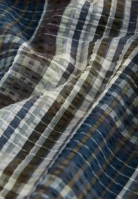 Textília s károvaným vzorom v námorníckej modrej, zelenej a béžovej farbe, s hladkou, ľahkou látkou, ktorá vykazuje jemné záhyby a vrásky.