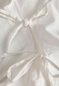 Κοντινή λήψη λευκού υφάσματος με υφή και δύο δεμένα φιόγκους κορδέλας, που δείχνει λεπτομερές ράψιμο και μαλακές πτυχές.