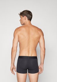 Schwarze Baumwoll-Boxershorts mit einem figurbetonten Design und elastischem Bund, von hinten betrachtet, was die glatte Textur und minimalen Nähte hervorhebt.