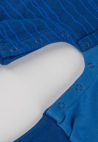 Indumento blu in misto di tessuti solidi e a righe, con bottoni a pressione lungo il collo e la spalla per una chiusura facile.