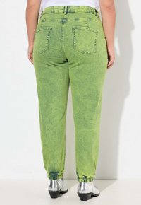 Pantalones verdes lima, holgados, con puños elásticos, cinco bolsillos y una textura desgastada. Zapatos plateados visibles en la parte inferior.