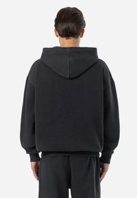 Black oversized hoodie with a large hood, ribbed cuffs, and hem, displaying a soft, textured fabric and minimal design. Back view shown.