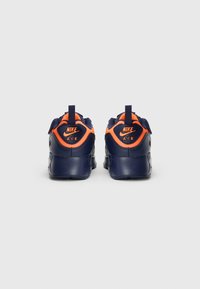Nike Air tenisice imaju gornji dio od sintetičkog materijala u tamnoplavoj boji s narančastim naglascima, podstavljeni ovratnik i teksturiranu potplat za bolji grip.