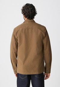 Brown canvas jacket with a collar, long sleeves, and button wrist closures. Features a smooth texture and a simple, clean design.