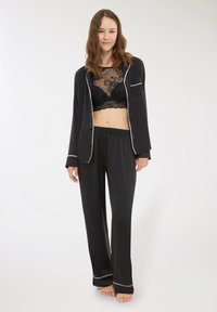 Completo pigiama in raso nero con camicia a bottoni bordata di bianco e pantaloni abbinati, accompagnati da un reggiseno in pizzo nero.