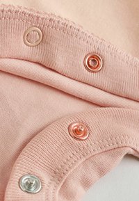 Primer plano de tela rosa claro con tres botones de presión metálicos en plata y oro rosa, mostrando detalles de costura y textura.