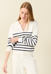 Weißer Pullover mit navyblauen horizontalen Streifen, V-Ausschnitt und Kragen-Design. Weicher Stoff, gerippte Bündchen und Saum, kombiniert mit hellen Hosen.