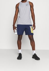 Camiseta sin mangas gris de Nike, pantalones cortos azul marino con un gran logo amarillo de "Nike", zapatillas deportivas negras y calcetines blancos con el swoosh negro de Nike.