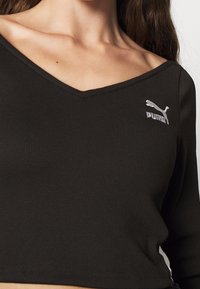 Top corto a maniche lunghe ribbed nero con scollatura a V e logo Puma argentato sul lato sinistro. Texture morbida con design aderente.