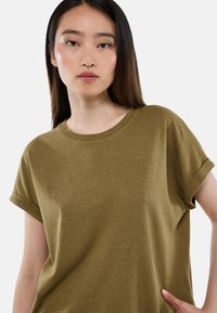 T-shirt olive à manches courtes avec un col rond et des manches retroussées, fabriqué en tissu cotonné texturé, présentant une coupe décontractée.
