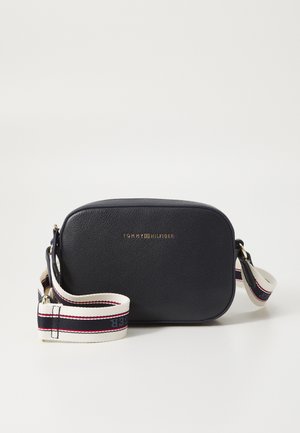 Petit sac bandoulière compact en cuir noir avec logo Tommy Hilfiger doré et sangle blanche réglable avec rayures bleu marine et rouges.