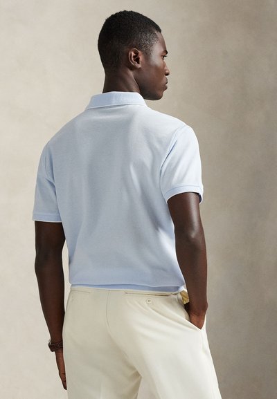 Lys blå kortermet polotrøye med myk tekstur og ribbestrikket krage, kombinert med kremfargede bukser med baklommer.