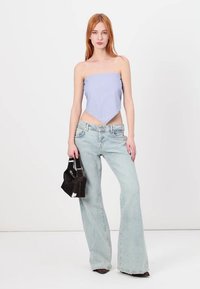 Pruhovaný bandeau top s špičatým lemem, doplněný světle modrými rozšířenými džíny. Modelka drží malou černou kabelku. Jednobarevné pozadí.