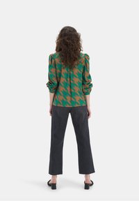 Blusa houndstooth verde e marrone con maniche arricciate, abbinata a jeans scuri con vita alta e sandali con tacco a blocco.