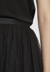 Gonna in tulle nera con sovrapposizione texturizzata e piccoli motivi ricamati, completata da una cintura in raso nero liscia.