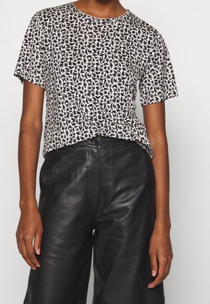 Persoon draagt een zwart-wit abstract patroon overhemd met korte mouwen, ingestopt in een hooggevoerde zwarte leren broek.