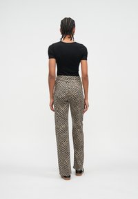 Čierne priliehavé tričko v kombinácii so širokými béžovo-hnedými pruhovanými nohavicami. Nohavice majú zadné vrecká a hladkú textúru.