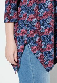 Dunkelblaue Bluse mit einem bunten abstrakten Muster in Rot und Blau, mit Dreiviertelärmeln und einem Verlaufsausschnitt.
