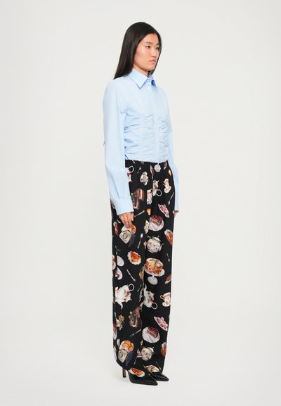 Cămașă turcoaz cu pliuri, asortată cu pantaloni largi negri, decorați cu imprimeuri colorate de mâncare și băuturi. Modelul poartă tocuri înalte.