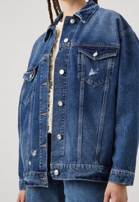 Jeansjacka i medelblått med en lätt blekt finish, med framfickor, silverknappar och slitna detaljer.