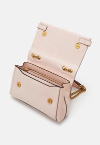 Sac à main en cuir texturé rose clair avec fermoirs à boutons dorés, bandoulière chaîne et rabat ouvert montrant les compartiments intérieurs.