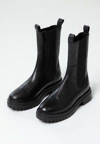 Stivali alla caviglia in pelle nera con finitura liscia, pannelli elastici ai lati e suola in gomma spessa. Presenta pratici anelli nella parte superiore per un facile indossamento.