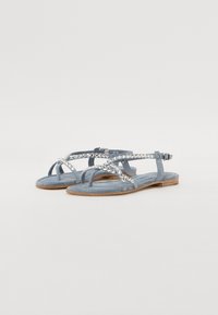 Sandales en suède bleu avec une semelle plate, comportant plusieurs brides et des embellissements en strass sur le dessus pour un détail supplémentaire.