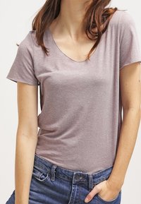 Ljust mauve kortärmad t-shirt med v-ringning, tillverkad av slätt tyg; matchad med blå denimjeans med klassisk passform.