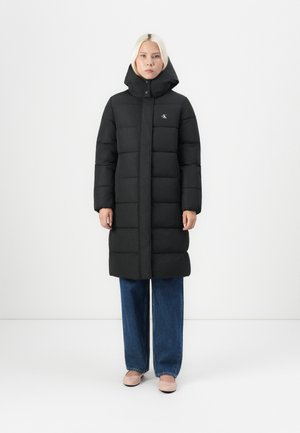 Black puffer coat with a high collar and front zipper, featuring quilted sections. Paired with wide-leg denim jeans and light-colored shoes.