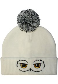 White knit beanie featuring embroidered owl eyes with yellow pupils, a ribbed band, and a black-and-white pom-pom on top.