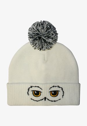White knit beanie featuring embroidered owl eyes with yellow pupils, a ribbed band, and a black-and-white pom-pom on top.