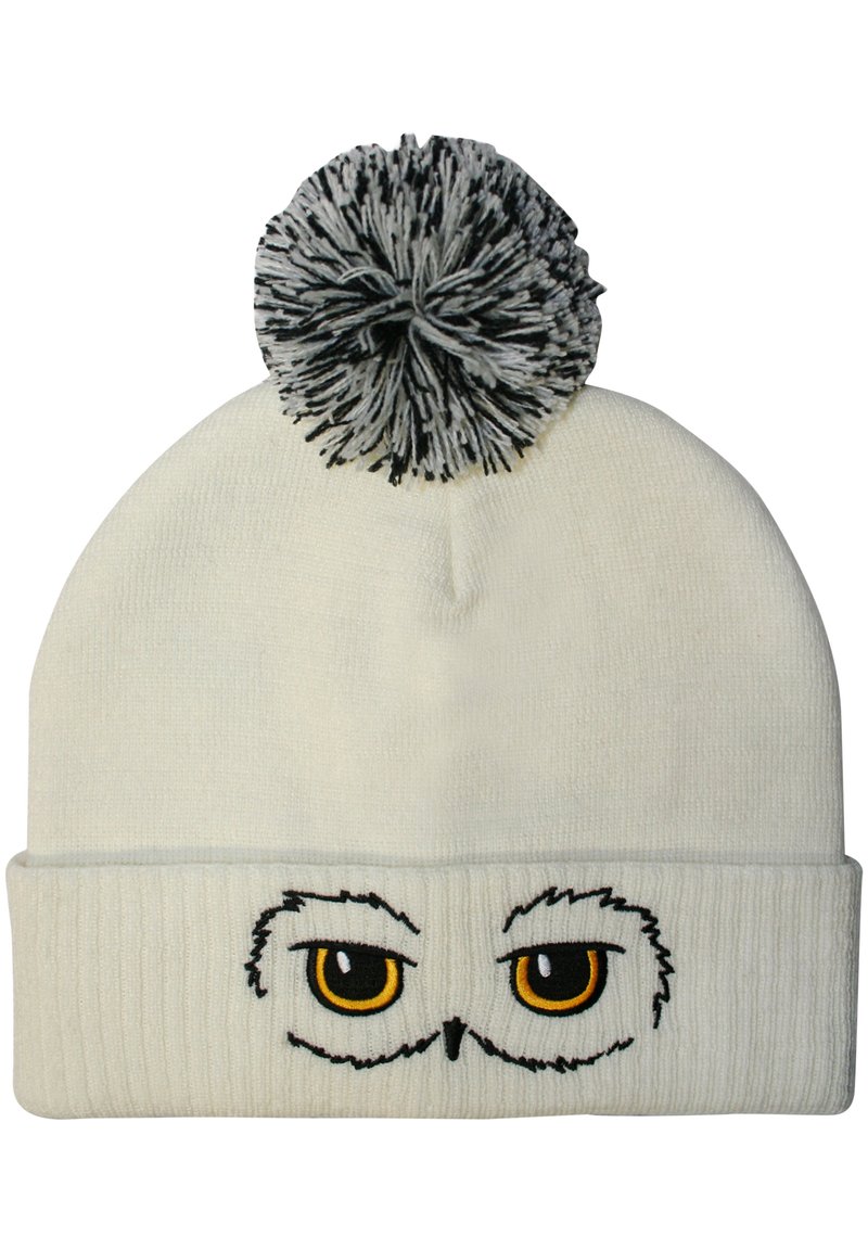 White knit beanie featuring embroidered owl eyes with yellow pupils, a ribbed band, and a black-and-white pom-pom on top.
