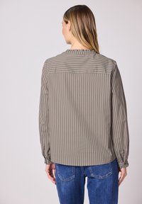 Blouse à rayures marron et blanches avec un col volanté et des manches ballon, associée à un jean en denim bleu.
