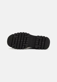 Black rubber shoe sole featuring a textured, patterned grip and pronounced tread design, designed for traction and durability.