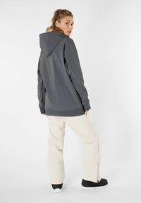 Graue Kapuzenjacke aus glattem Stoff, kombiniert mit hellbeigen Hosen. Schwarze Schuhe mit weißen Sohlen. Rückansicht, minimalistisches Design.
