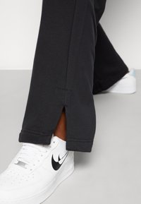 Czarne spodenki sportowe o luźnym kroju z rozcięciami na końcach, zestawione z białymi trampkami z czarnym logo swoosh.