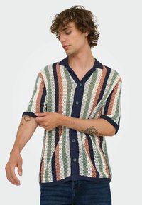Camisa de manga corta, de botones, con un patrón de rayas multicolores en verde, melocotón y azul marino, que presenta un material de punto texturizado y un cuello sólido.