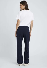 Pantalons larges navy en tissu doux, avec une texture lisse et deux poches arrière. Accompagnés d'un t-shirt blanc uni.