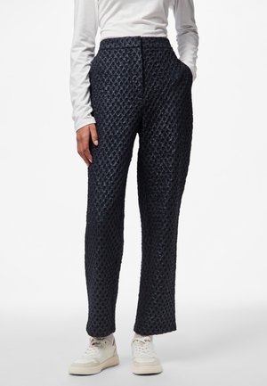 Pantalons en bleu marine texturés à taille haute, avec une jambe droite et des poches latérales, associés à des baskets blanches.