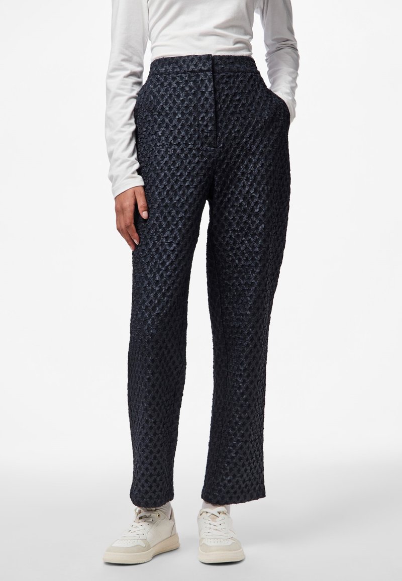 Pantaloni in blu navy con texture, a vita alta, dotati di gamba dritta e tasche laterali, abbinati a sneakers bianche.
