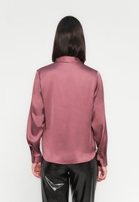 Camisa de seda de mangas longas em mauve, com colarinho e punhos botões, tendo uma textura suave e uma bainha curva. Vista traseira mostrada.