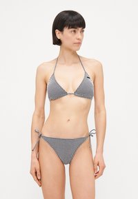 Melnbalts šaha raksts bikini ar trīsstūra augšdaļu un sasietām jostas saitēm, ar gludu tekstūru un minimālu metāla detaļu daudzumu.
