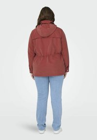 Giacca rossa con cappuccio, cintura con cordino, polsini con bottoni e inserti sul retro. Abbinata a jeans azzurri e sneakers bianche.