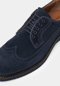 Navy semišové brogue boty s detailním perforováním, zakřiveným šitím a šesti dírkami na šněrování. Silná podrážka s kontrastním okrajem.