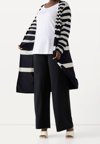 Modrý a bílý pruhovaný kardigan s otevřeným předním dílem, nošený přes bílou košili a černé kalhoty s širokými nohavicemi, doplněný bílými sandály. Hladká textura.