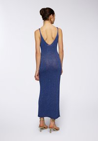 Abito maxi glitterato blu con profondo scollo a V sul retro, dotato di spalline sottili e silhouette aderente. L'orlo è leggermente sfilacciato. Include scarpe con tacco coordinate.