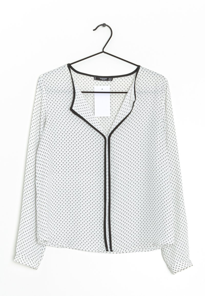 Blouse blanche à manches longues avec petit motif géométrique noir et bordure noire, suspendue sur un cintre noir sur fond blanc.